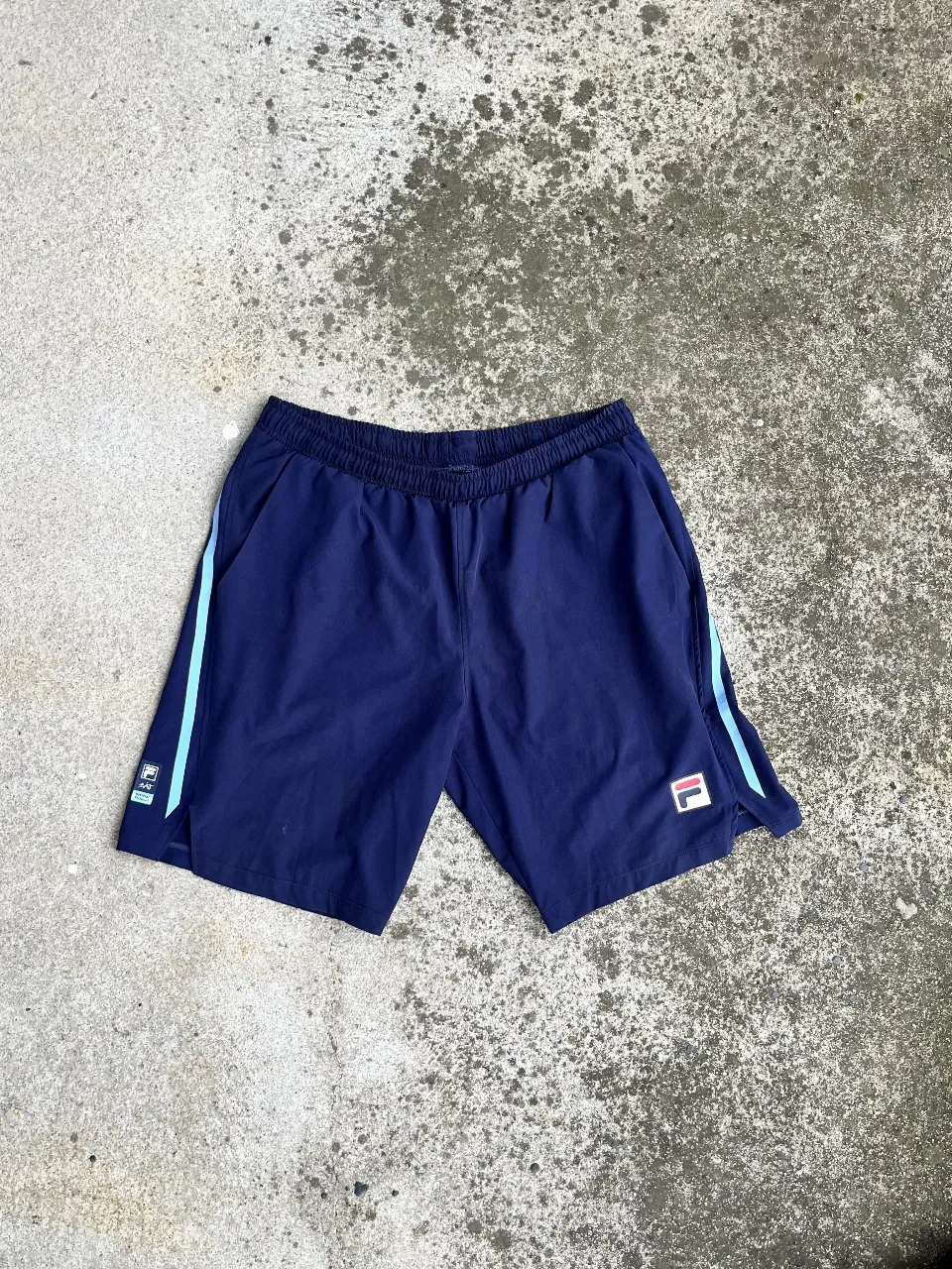 Short deportivo Fila azul marino con detalles celestes. Ideal para actividades físicas o uso casual. Cuenta con el logo de la marca.