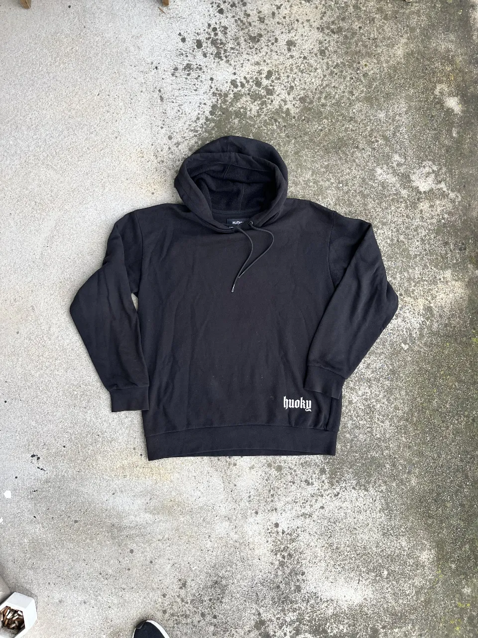 Buzo canguro negro con capucha y el logo de "huoky" en la parte delantera y trasera. Ideal para un look urbano y casual.