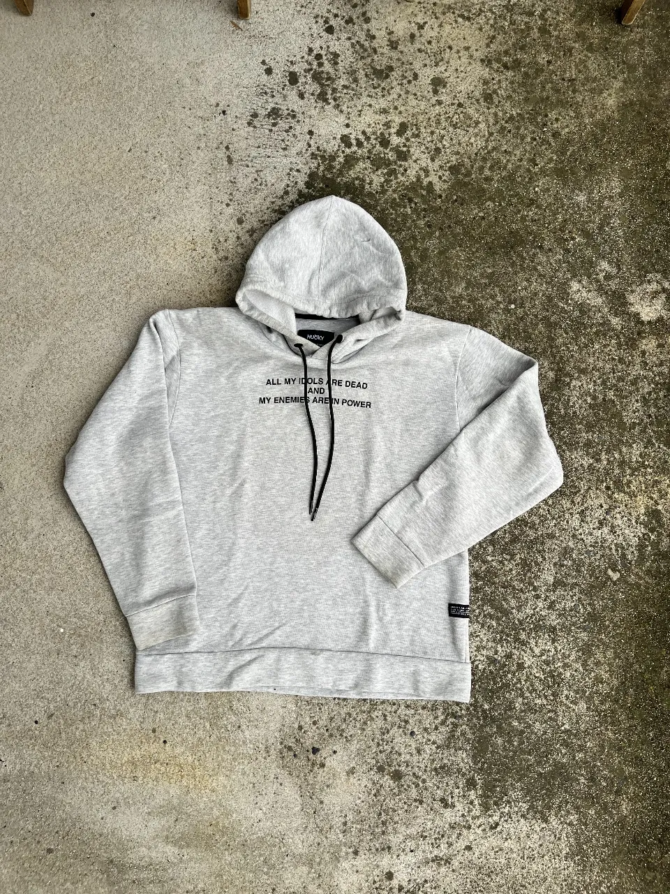 Buzo canguro gris con capucha y estampado en la parte delantera y trasera. Diseño streetwear con frases y detalles gráficos.