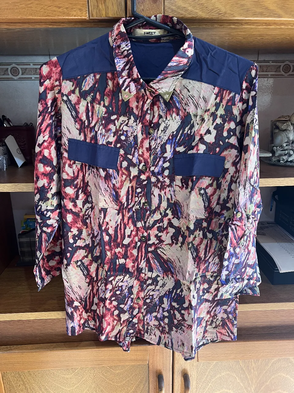 Camisa estampada para mujer, con diseño abstracto en tonos rojos, azules y blancos. Cuello y detalles en azul marino. Ideal para un look casual y con estilo.