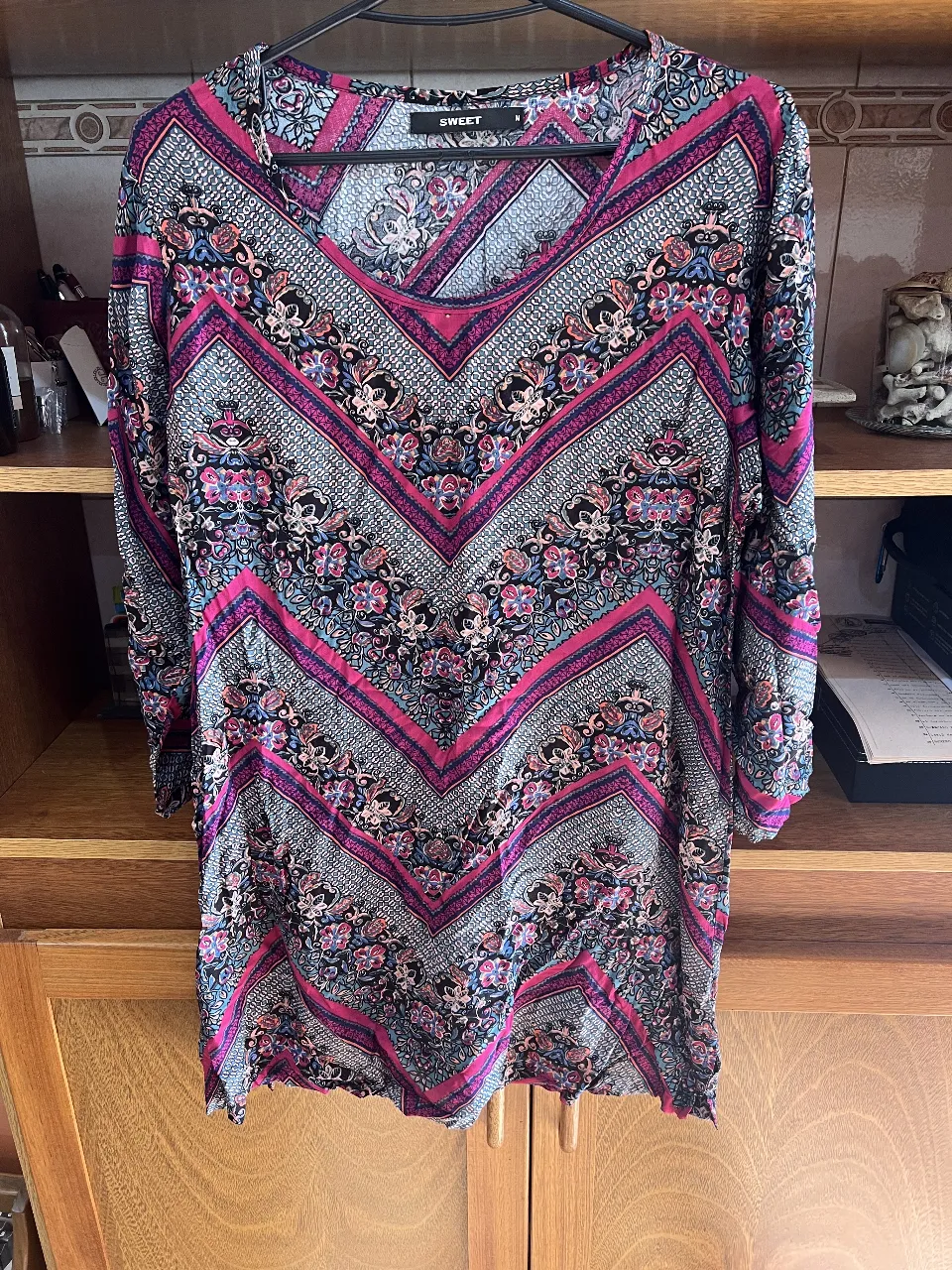 Vestido midi con estampado geométrico en tonos rosa, negro y gris. Cuello en V y mangas 3/4. Ideal para un look casual y cómodo.