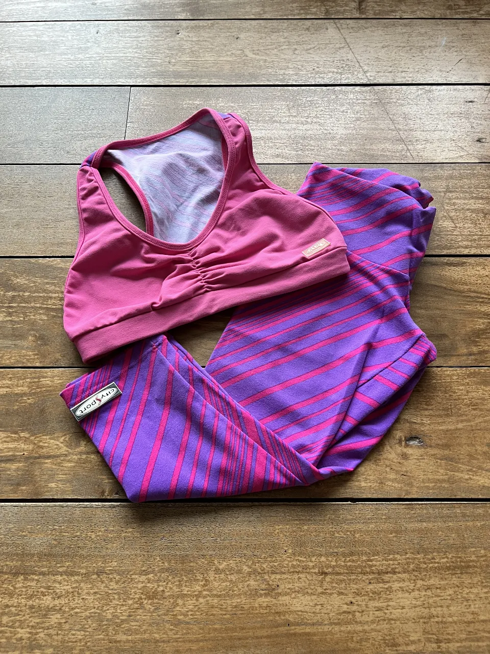 Conjunto deportivo para mujer, compuesto por un top y calzas. El top es de color rosa y las calzas tienen un diseño a rayas en tonos violeta y rosa. Ideal para actividades físicas.