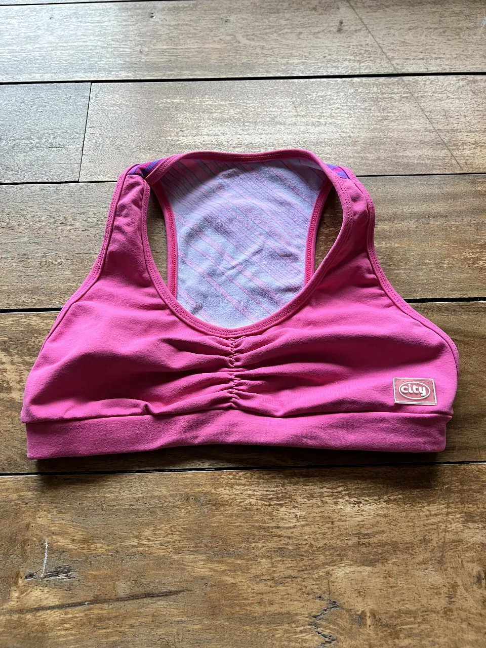 Top deportivo rosa con detalles en violeta. Ideal para actividades de bajo impacto. Diseño con fruncido en el frente y espalda deportiva.