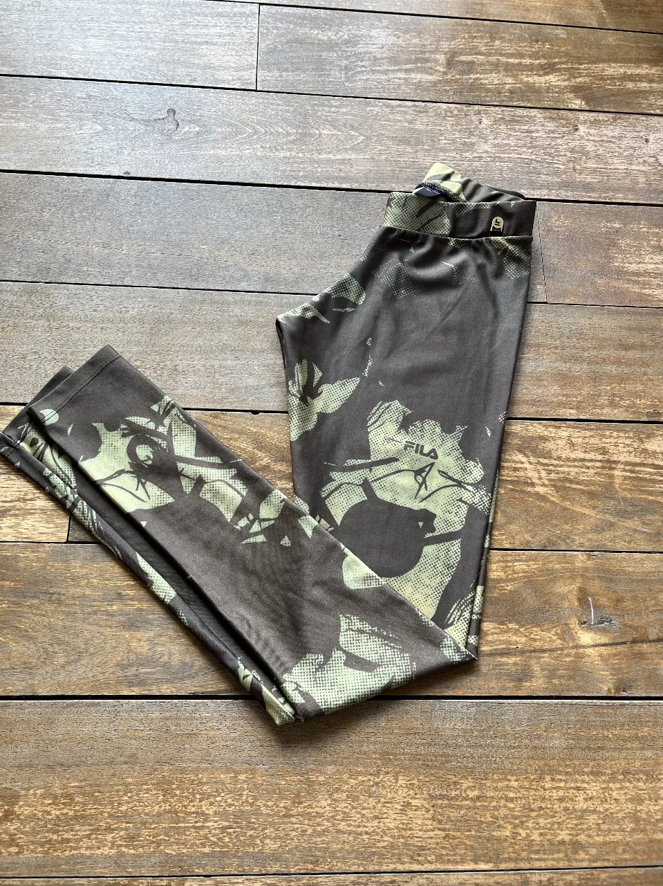 Calzas deportivas Fila con estampado camuflado en tonos marrones y verdes. Ideal para actividades físicas o un look casual.