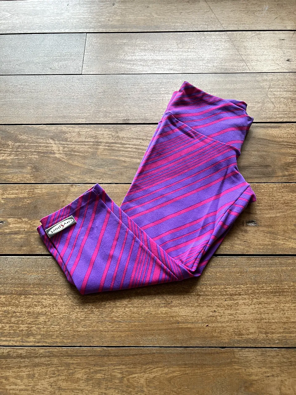 Calzas deportivas de mujer, con estampado a rayas diagonales en tonos violeta y rosa. Ideales para actividades físicas.