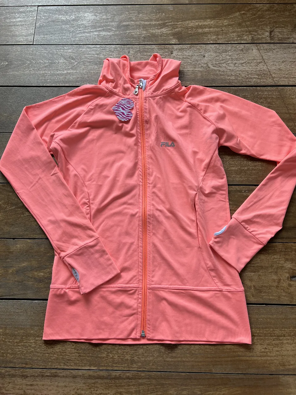 Buzo deportivo con cierre y capucha para mujer, color durazno. Con logo de la marca Fila estampado en el pecho. Ideal para actividades deportivas o uso casual.