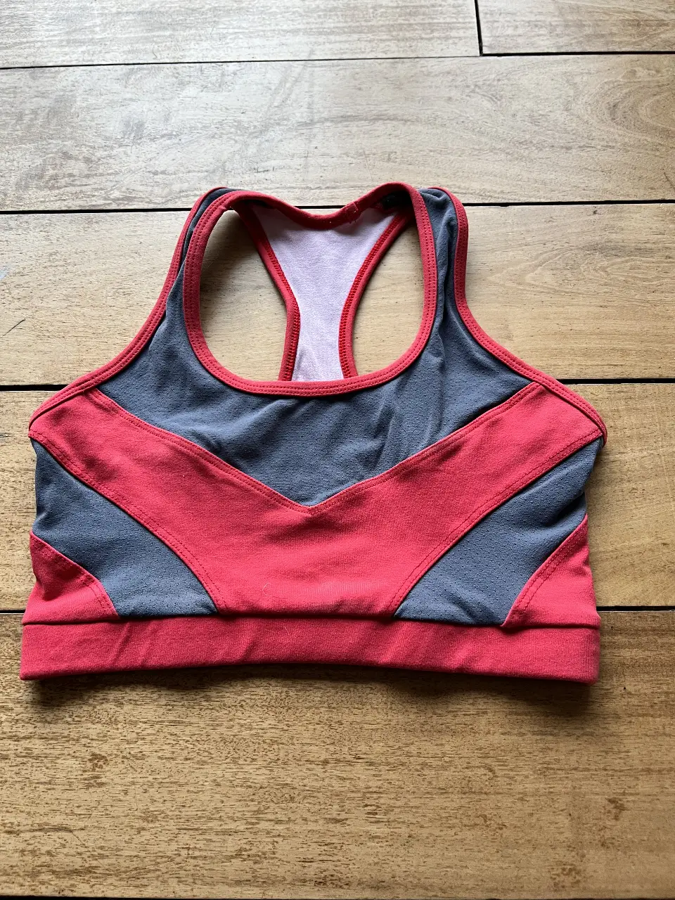 Top deportivo para mujer, con diseño en dos tonos, gris y rojo. Ideal para actividades de gimnasio y running. Confeccionado con materiales que brindan comodidad y soporte.