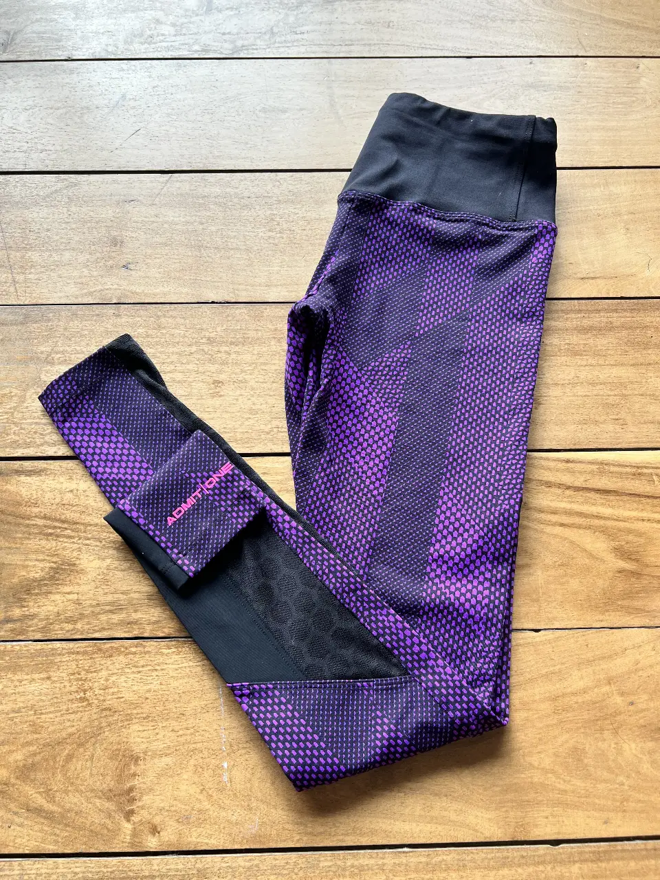 Calzas deportivas de mujer, con diseño geométrico en tonos violeta y negro. Posee detalles en negro y el logo de la marca en un lateral. Ideal para actividades físicas.