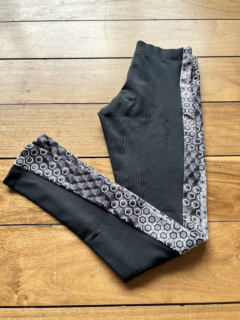 Calzas deportivas negras con detalles geométricos en los laterales. Perfectas para entrenar o para un look casual y cómodo.