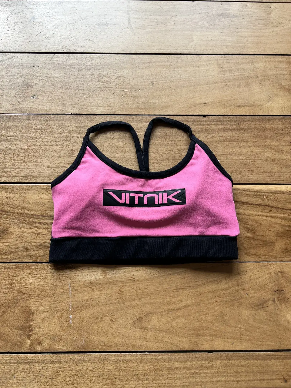Top deportivo de mujer, color negro y rosa, con espalda descubierta y logo de la marca. Ideal para entrenamientos de alto impacto.