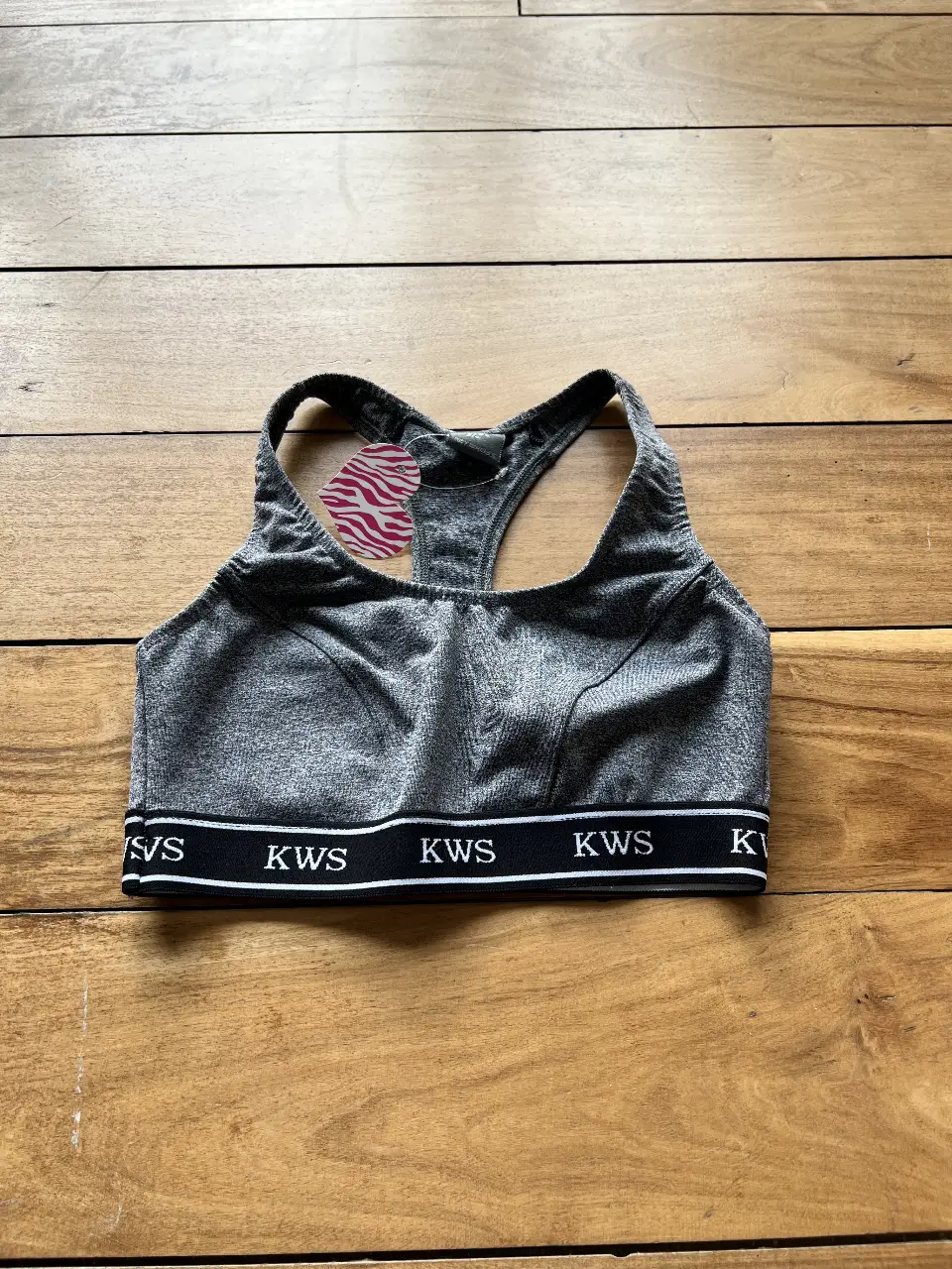 Top deportivo gris con banda inferior negra y detalles blancos. Ideal para entrenamientos y actividades físicas.