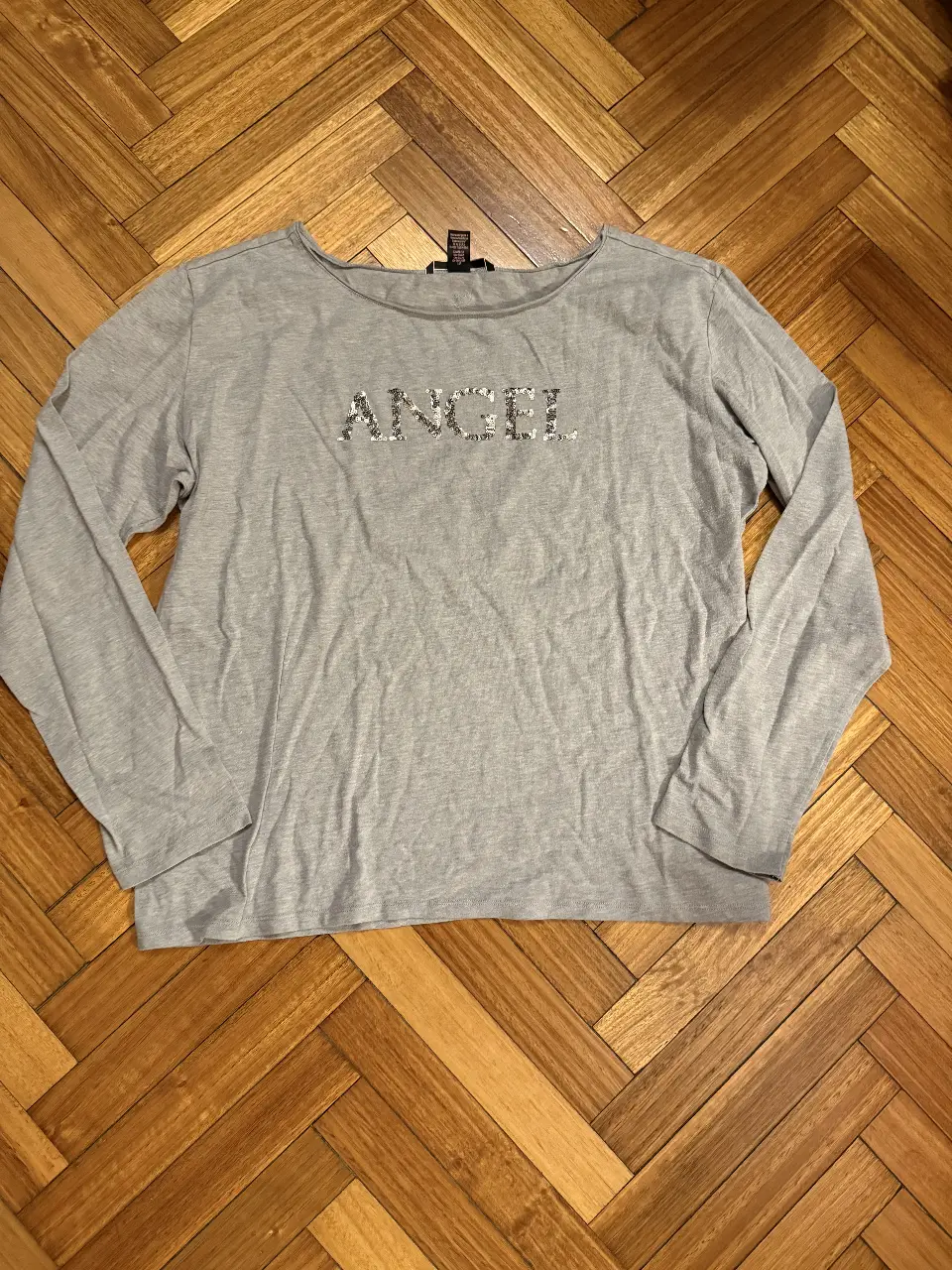 Remera manga larga gris de Victoria's Secret con la palabra 'ANGEL' en lentejuelas plateadas. Ideal para un look casual y cómodo.