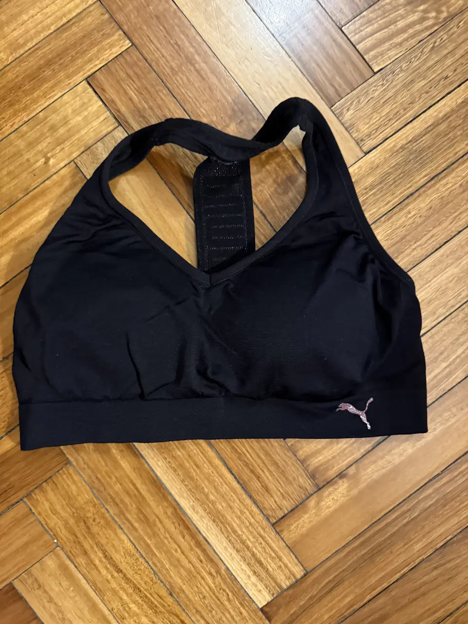 Top deportivo Puma negro con detalle del logo en rosa. Ideal para entrenamientos de alto impacto.