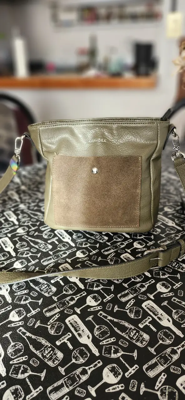 Cartera bandolera Amphora de cuero sintético color verde con bolsillo frontal de gamuza marrón y detalle de botón plateado. Ideal para un look casual y moderno.