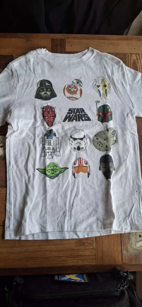 Remera blanca de niño con estampado de personajes de Star Wars. Diseño con Darth Vader, BB-8, Yoda y otros personajes icónicos. Ideal para fans de la saga.