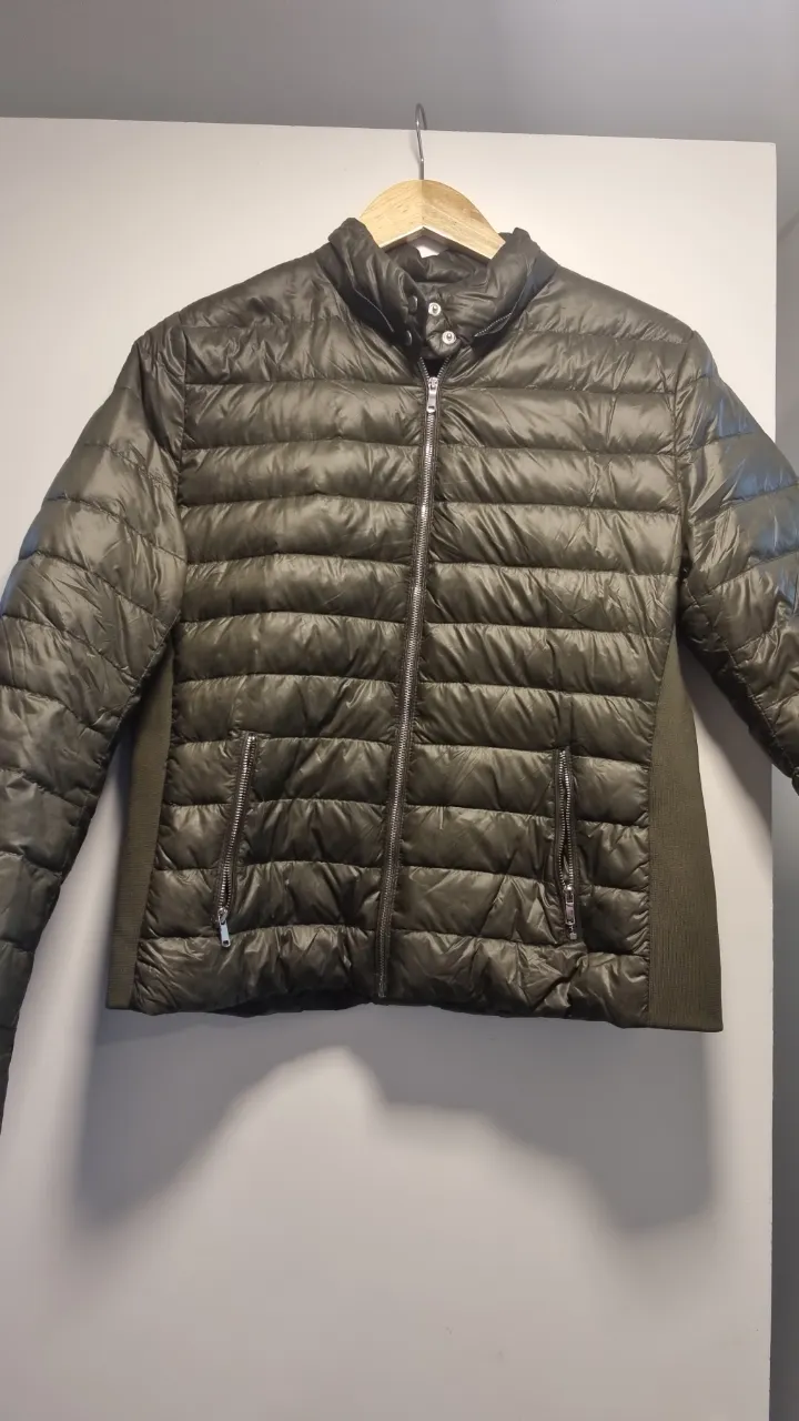 Campera de pluma acolchada para mujer, color verde oscuro. Diseño con cierre frontal, cuello alto y bolsillos con cierre. Ideal para el invierno.
