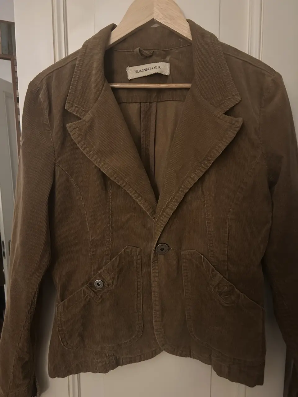 Blazer de corderoy marrón de la marca Rapsodia. Corte clásico con dos bolsillos delanteros y un botón para cerrar. Ideal para un look casual o para darle un toque elegante a tu outfit.