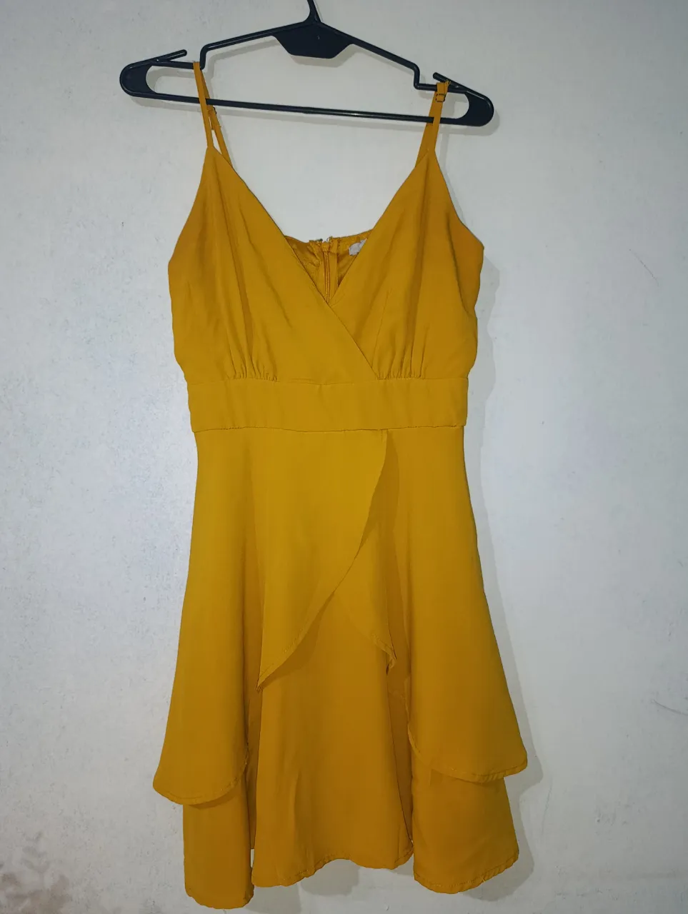 Vestido amarillo mostaza con breteles finos y escote cruzado. Posee un detalle de volados en la falda, dándole un toque moderno y femenino. Ideal para eventos de día o salidas.