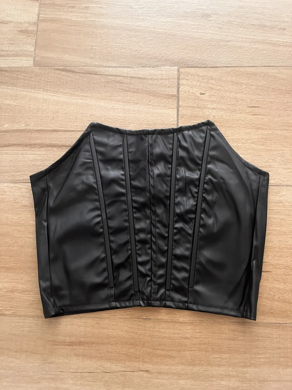 Top negro de cuero sintético con ballenas verticales en el frente y cierre en la espalda.