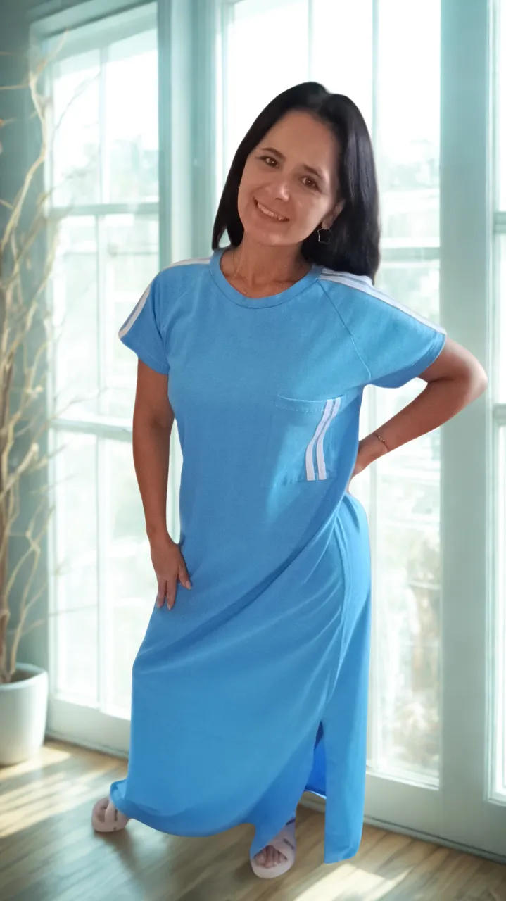 Vestido largo celeste de jersey de algodón, con cuello redondo y mangas cortas. Posee tajos laterales y detalles de tiras blancas en las mangas y en un bolsillo lateral. Ideal para un look casual y cómodo.