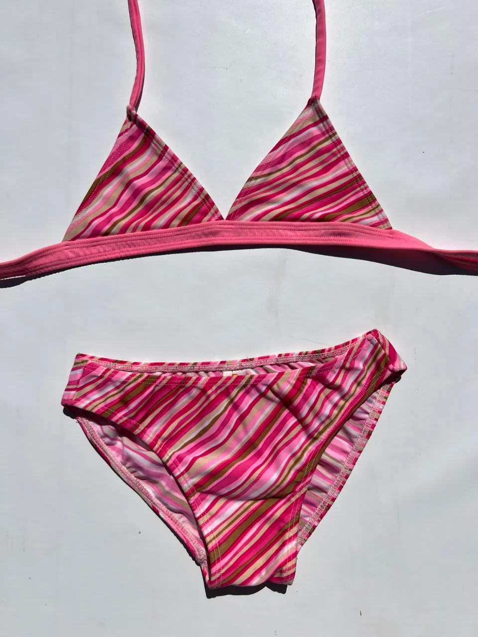 Conjunto de bikini estampado a rayas rosas, fucsias y marrones. El corpiño es triangular con tiras finas y el bombachón es clásico. Ideal para días de sol y playa.