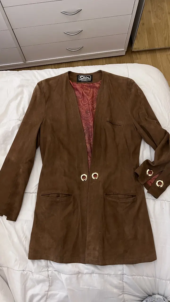 Chaqueta de gamuza marrón con forro interior estampado. Detalles dorados en los puños y cierre frontal. Ideal para un look vintage y elegante. hombros 41, mangas 60, largo 83