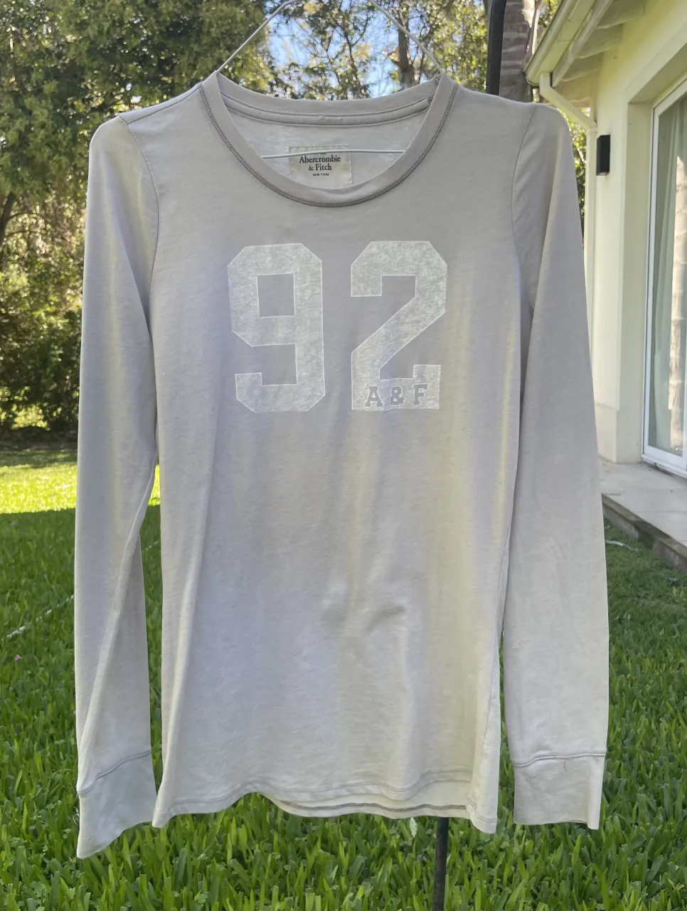 Remera gris de manga larga con estampa de números "92" y logo "A&F" en el frente. Cuello redondo y costuras grises.