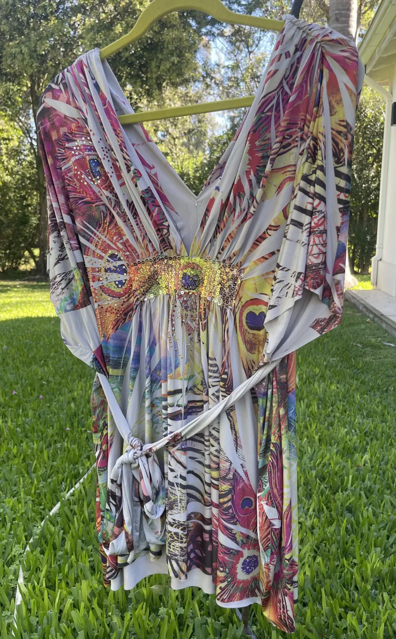 Vestido corto con estampado vibrante de plumas y detalles de lentejuelas y pedrería en la cintura. Posee un cinturón de tela a tono anudado.