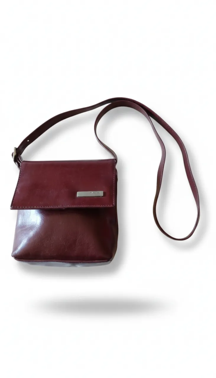 Cartera chica vintage color bordó, con correa regulable y detalle metálico con el logo de la marca. Sin bolsillos internos.