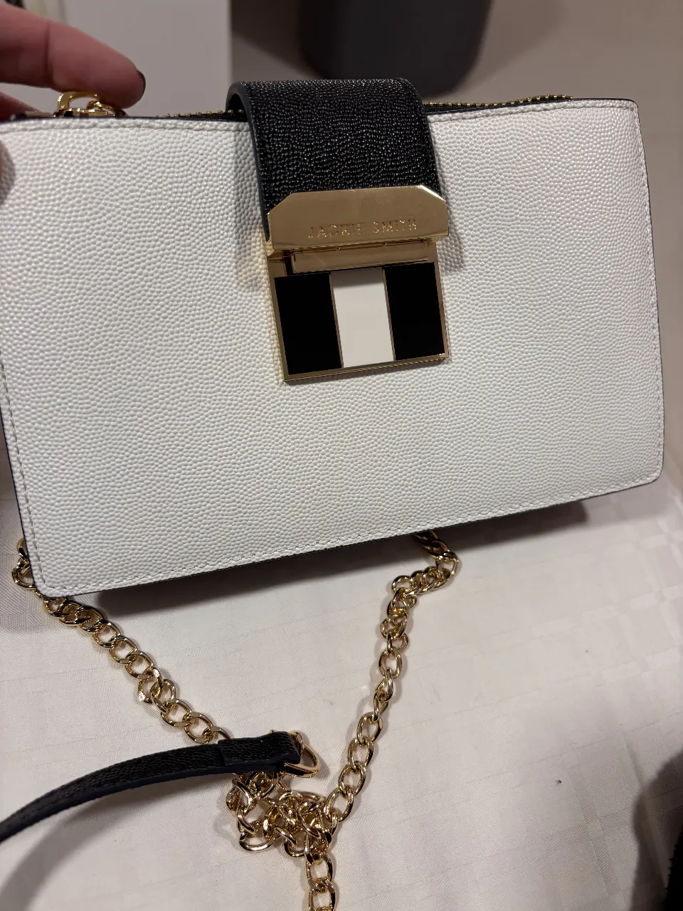 Cartera Jackie Smith de cuero sintético, color blanco y negro, con detalles dorados y cadena. Ideal para salidas y eventos.
