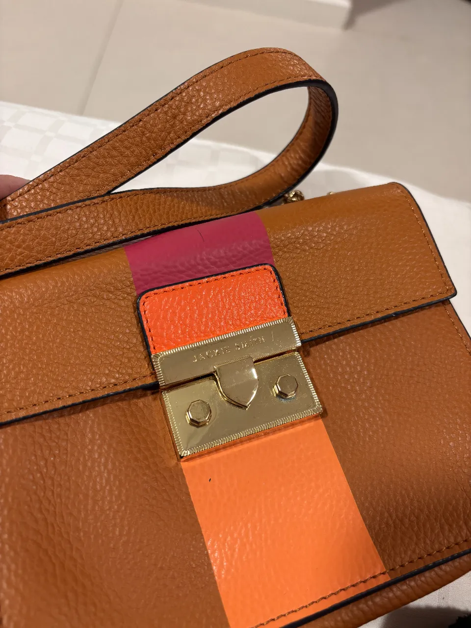 Cartera Jackie Smith de cuero marrón con detalles en naranja y rosa. Diseño elegante con cierre dorado y correa para llevar al hombro. Ideal para un look sofisticado.