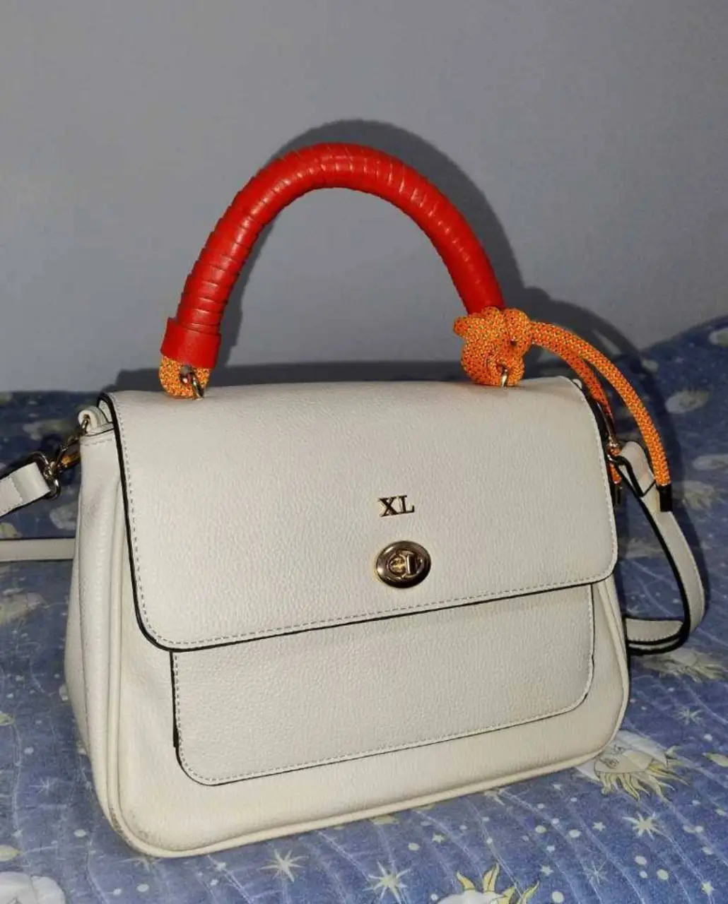 Cartera blanca con manija y detalles en rojo y naranja. Ideal para un look casual y moderno. Cuenta con correa para llevar al hombro y un interior espacioso.