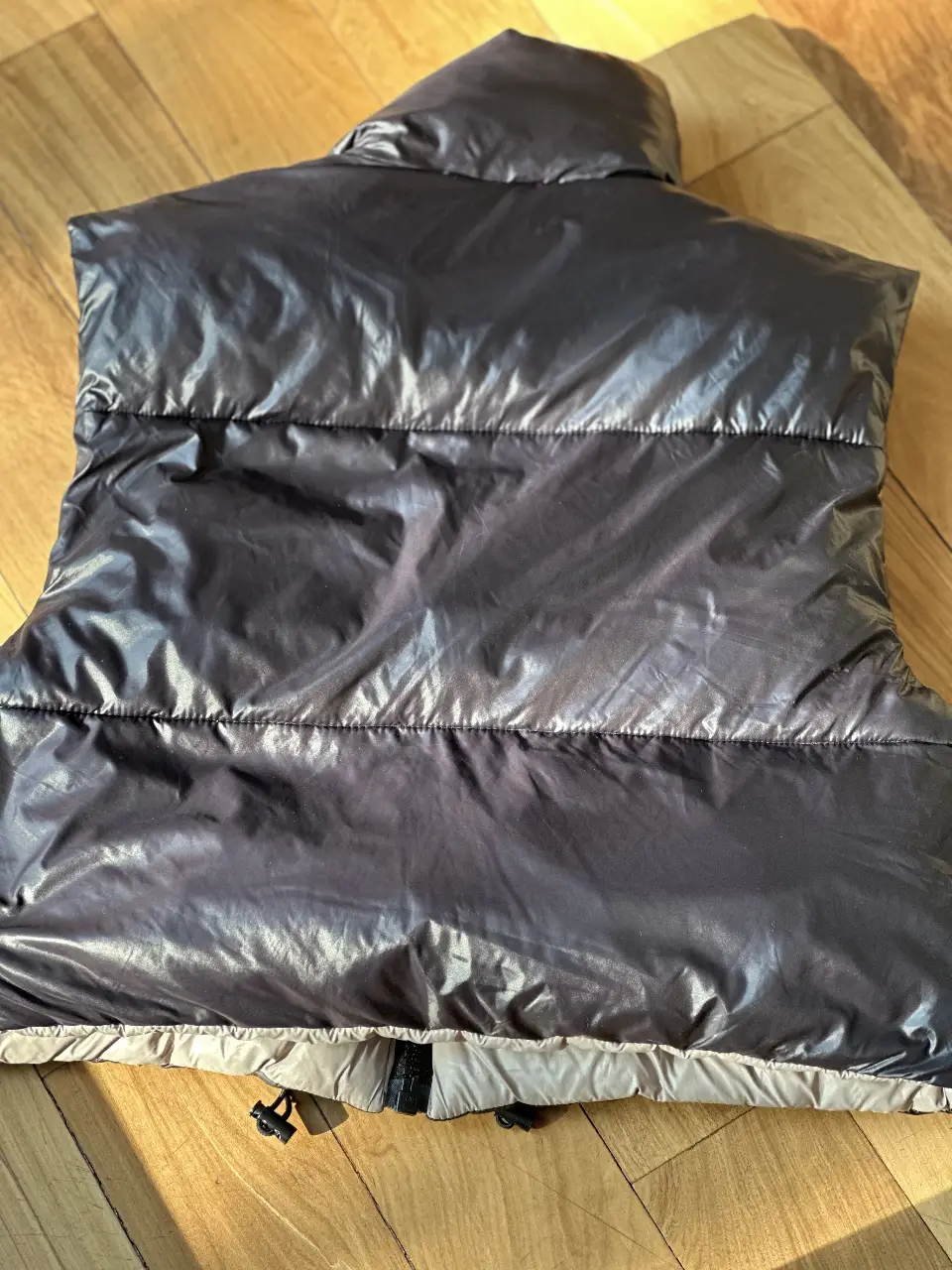 Chaleco reversible acolchado, ideal para el invierno. Un lado es gris oscuro brillante y el otro es beige claro. Tiene cierre y cuello alto.