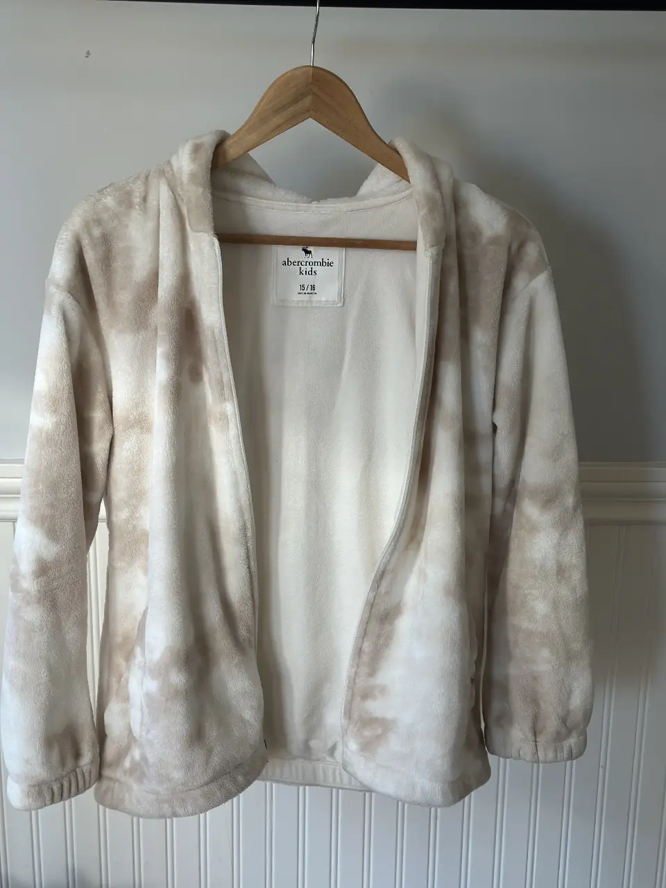 Buzo con cierre para niña, de polar, con estampado tie dye en tonos blanco y marrón. Posee capucha y bolsillos delanteros. Ideal para el invierno.