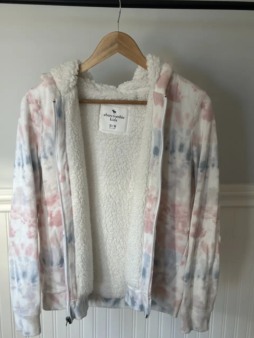 Buzo con cierre Abercrombie Kids para niña, con diseño tie dye en tonos rosa, celeste y blanco. Interior de sherpa suave y abrigado. Ideal para un look casual y cómodo.