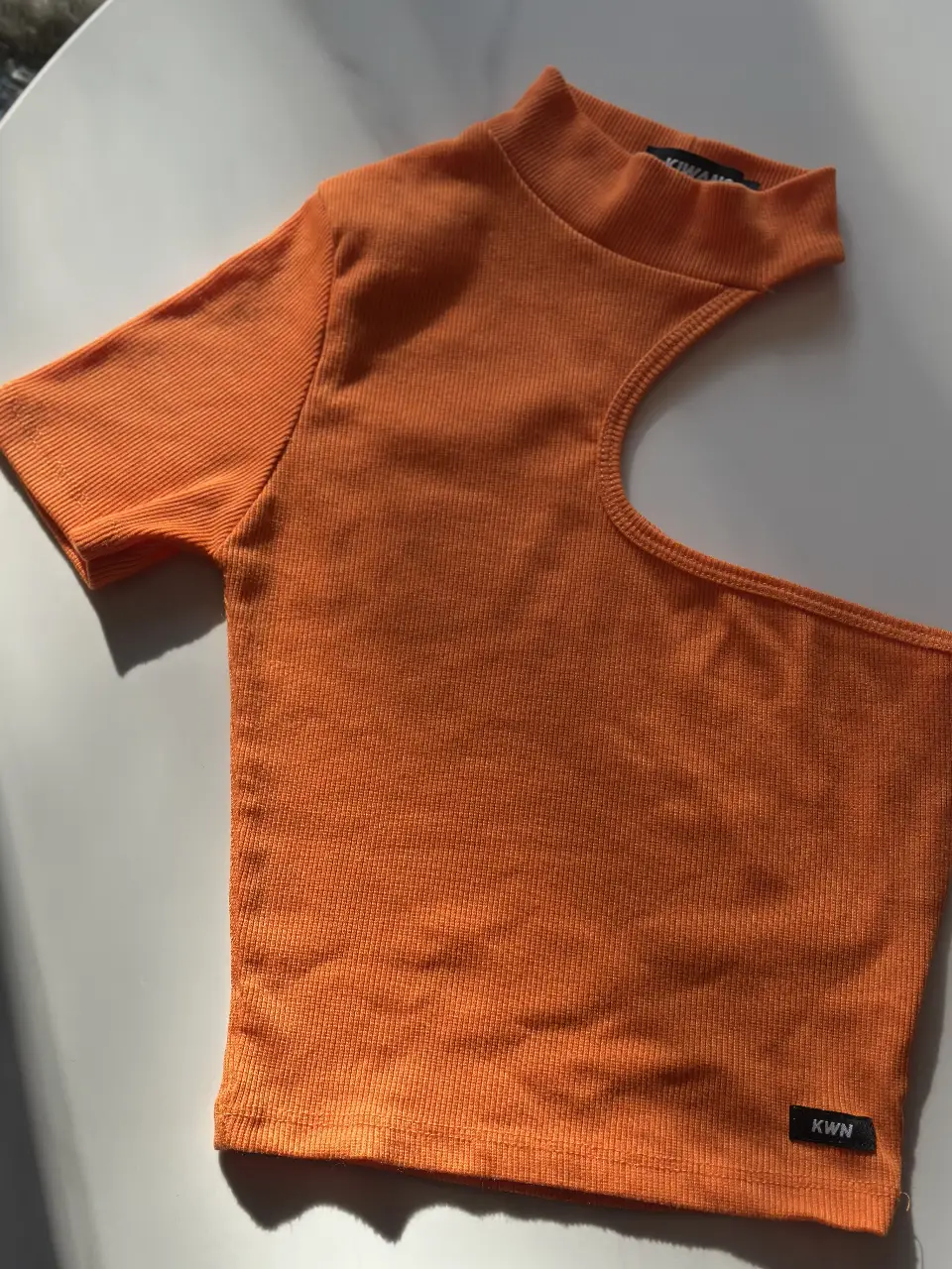 Top naranja con un hombro descubierto y cuello alto. Ideal para un look moderno y audaz. Perfecto para combinar con jeans o faldas.