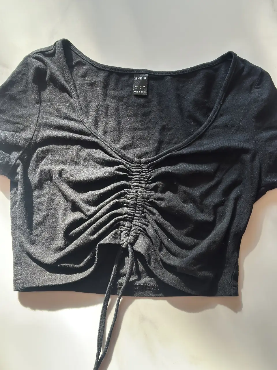 Top negro corto con fruncido en el frente y detalle de ajuste. Ideal para un look casual y moderno.