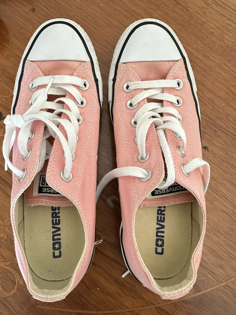 Zapatillas bajas de lona color rosa con cordones blancos y detalles en negro. La suela es blanca con una línea negra.
