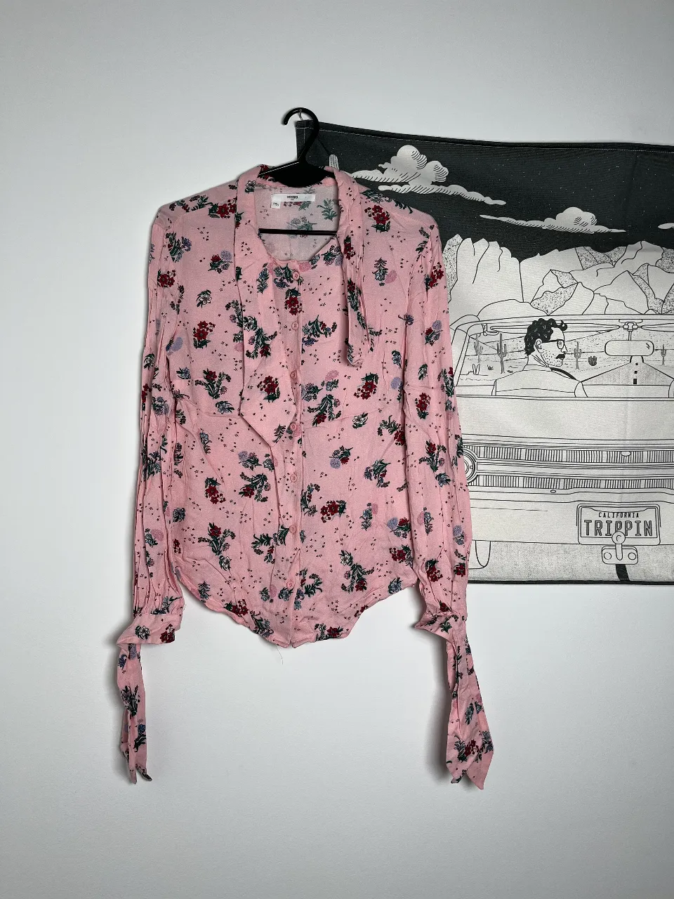 Blusa de mujer con estampado floral en tonos rosas y detalles en verde y rojo. Diseño con cuello con lazo y mangas largas con puños anudados. Ideal para un look romántico y femenino.