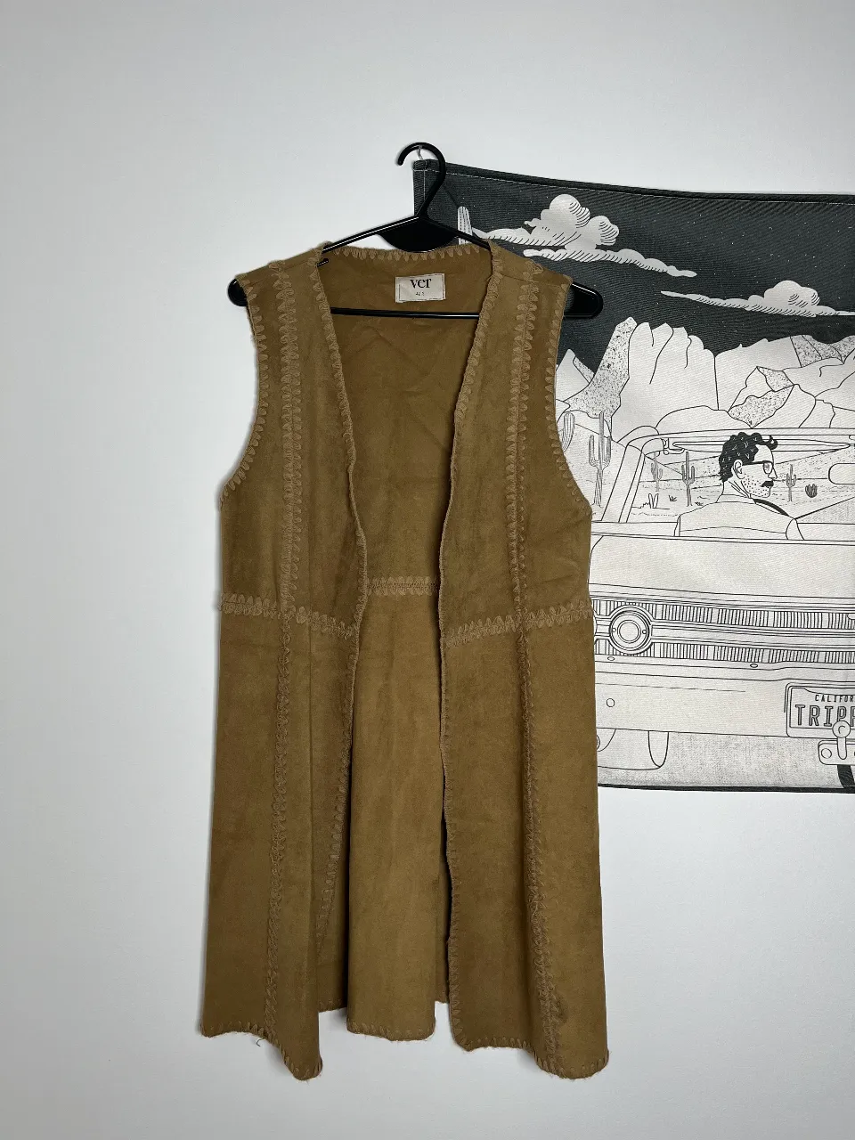 Chaleco largo de gamuza sintética en tono marrón. Diseño sin mangas con detalles de costuras decorativas. Ideal para un look boho o casual.