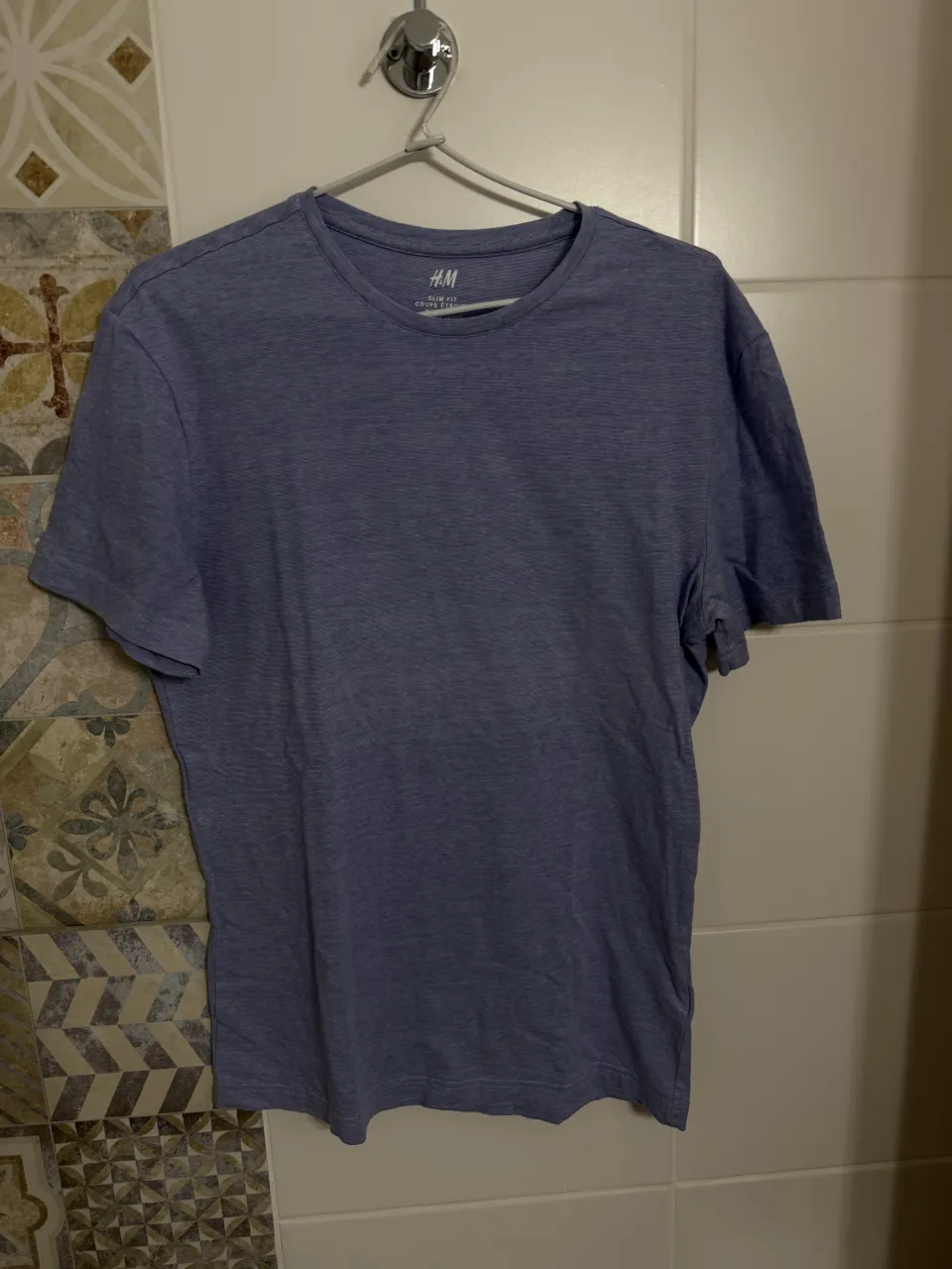 Remera de manga corta de color azul claro con finas rayas horizontales. Cuello redondo.