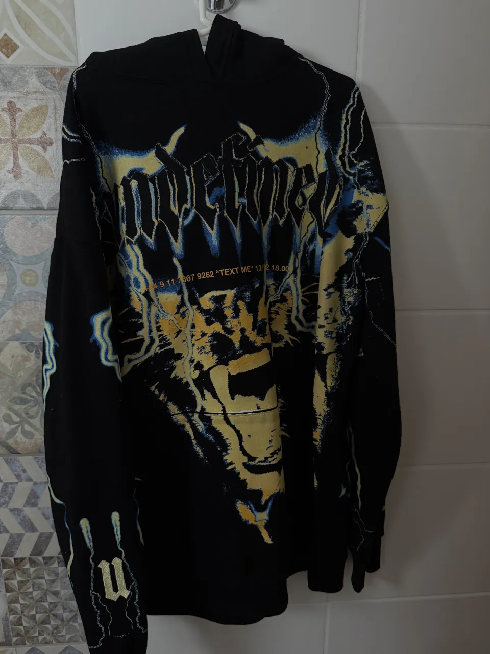 Buzo negro con capucha y estampa gráfica de un felino y rayos en tonos amarillos, azules y blancos. Posee estampa de texto en la manga y en la espalda.