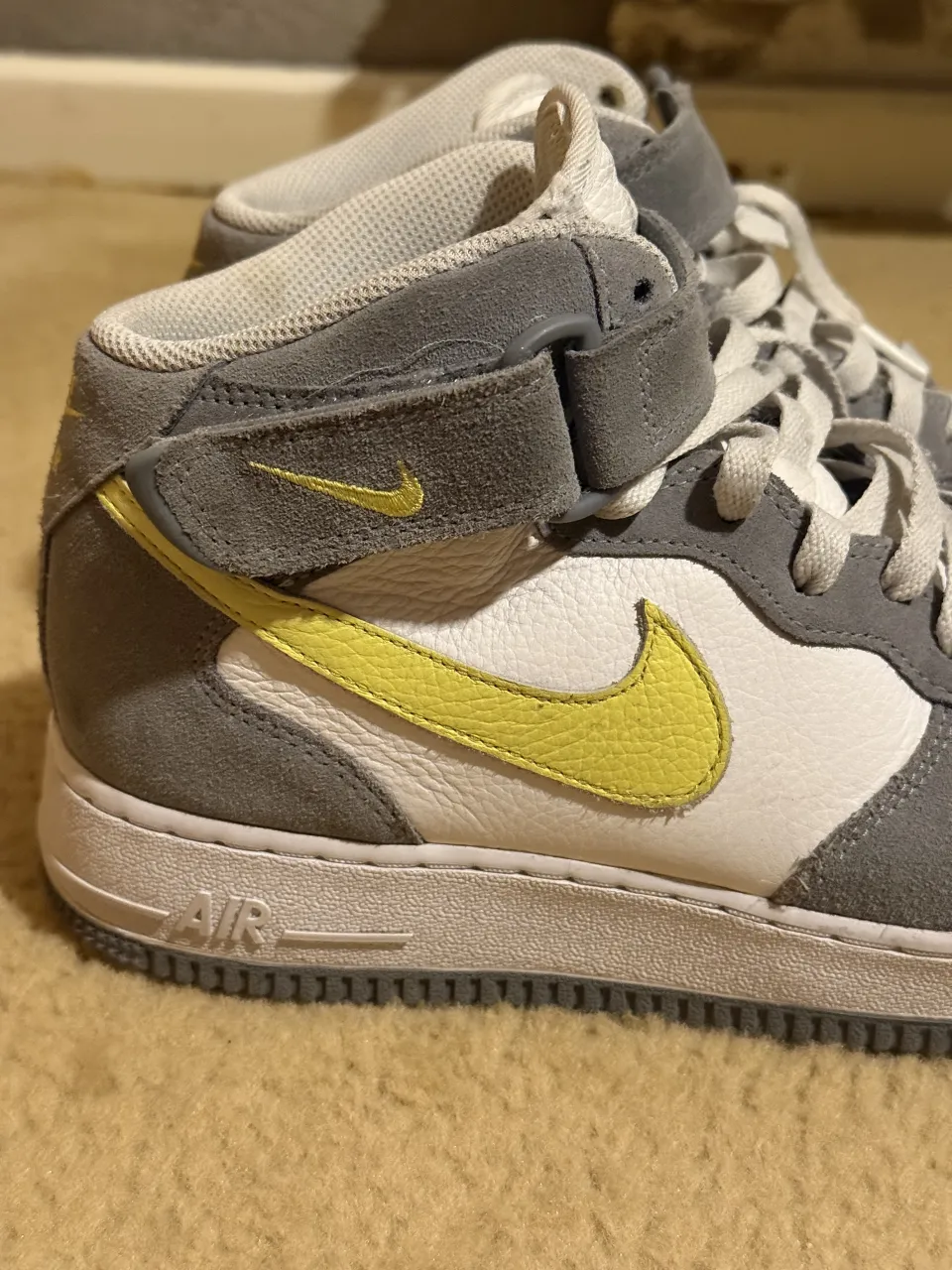 Zapatillas Nike Air Force 1 Mid, grises con detalles en blanco y swoosh amarillo. Cierre de velcro en el tobillo.