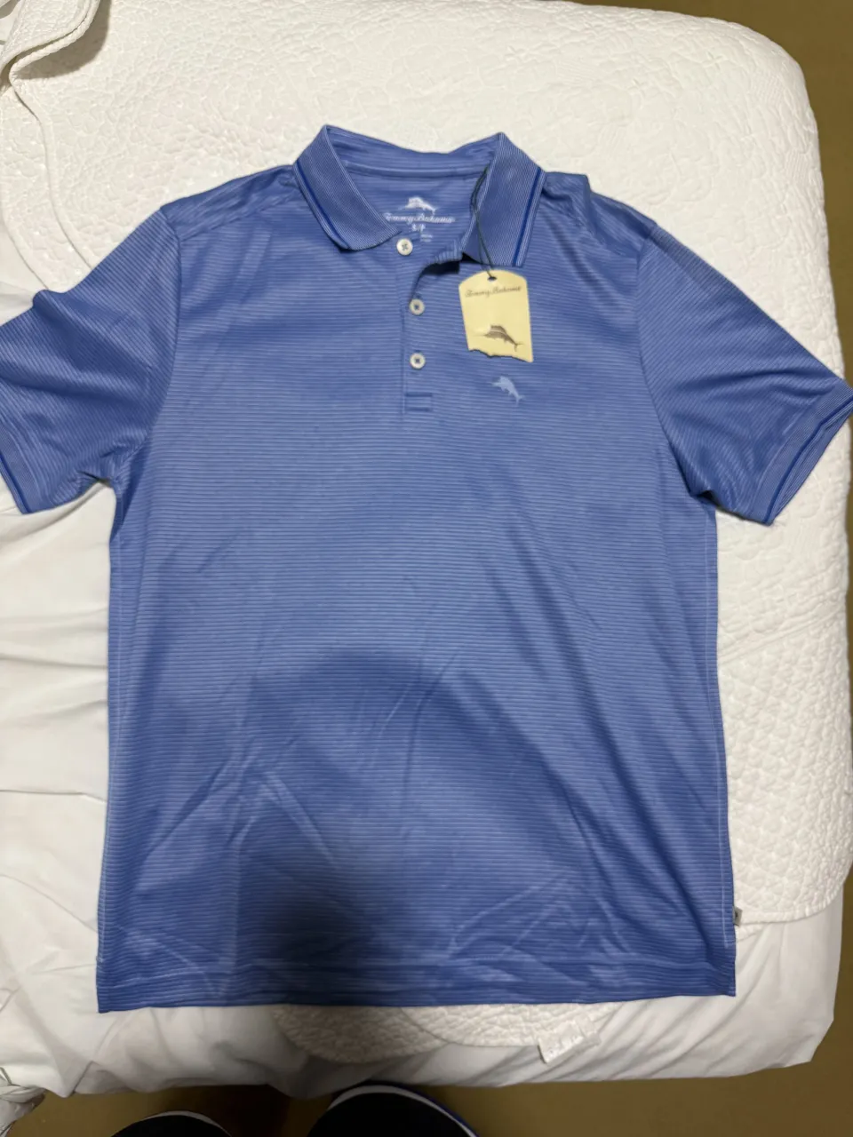 Remera polo azul con finas rayas blancas horizontales. Tiene cuello camisero y tres botones en la parte superior.