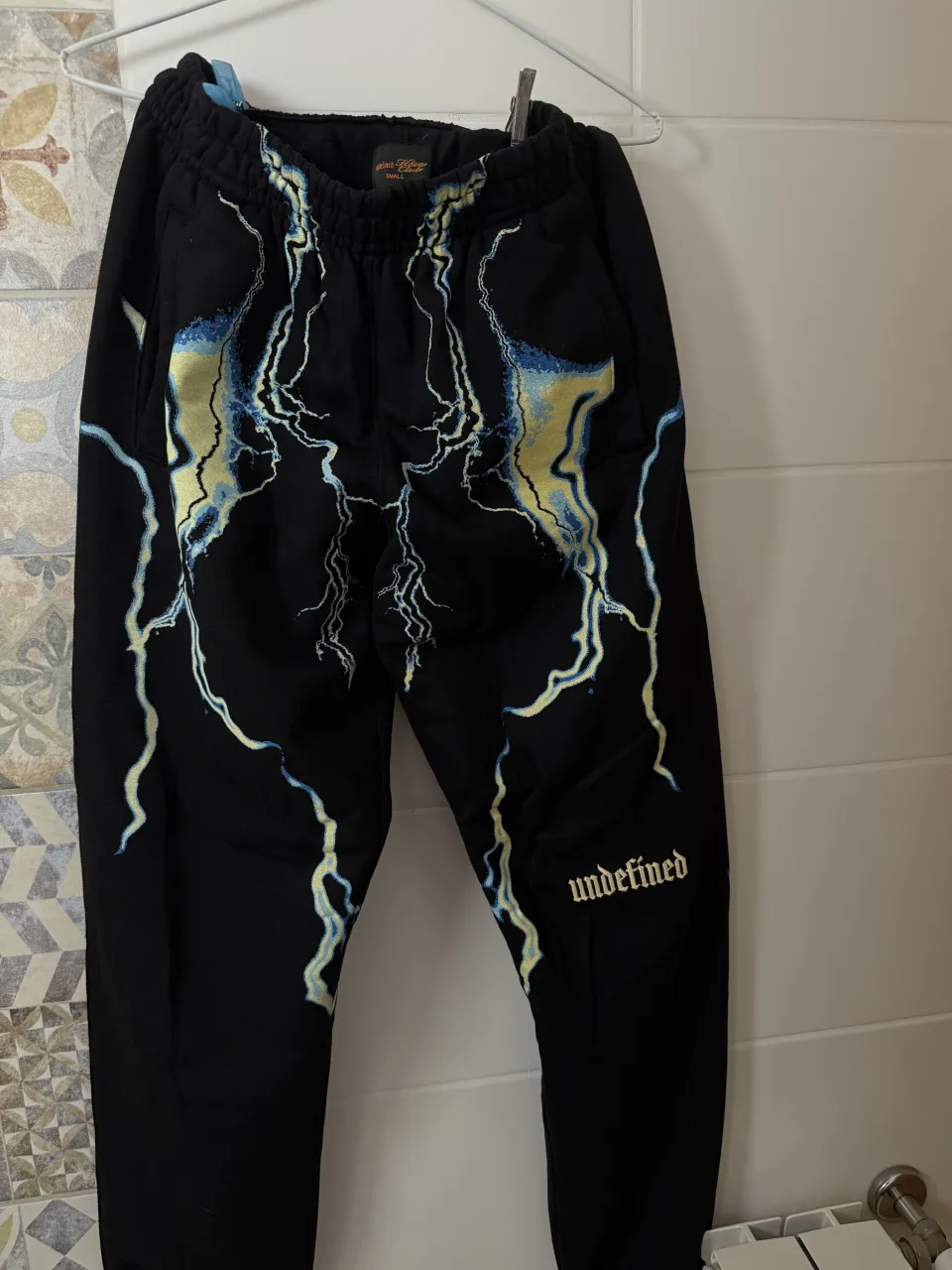 Pantalón de algodón negro con estampa de rayos en amarillo y azul. Posee la palabra "undefined" bordada en la pierna izquierda.