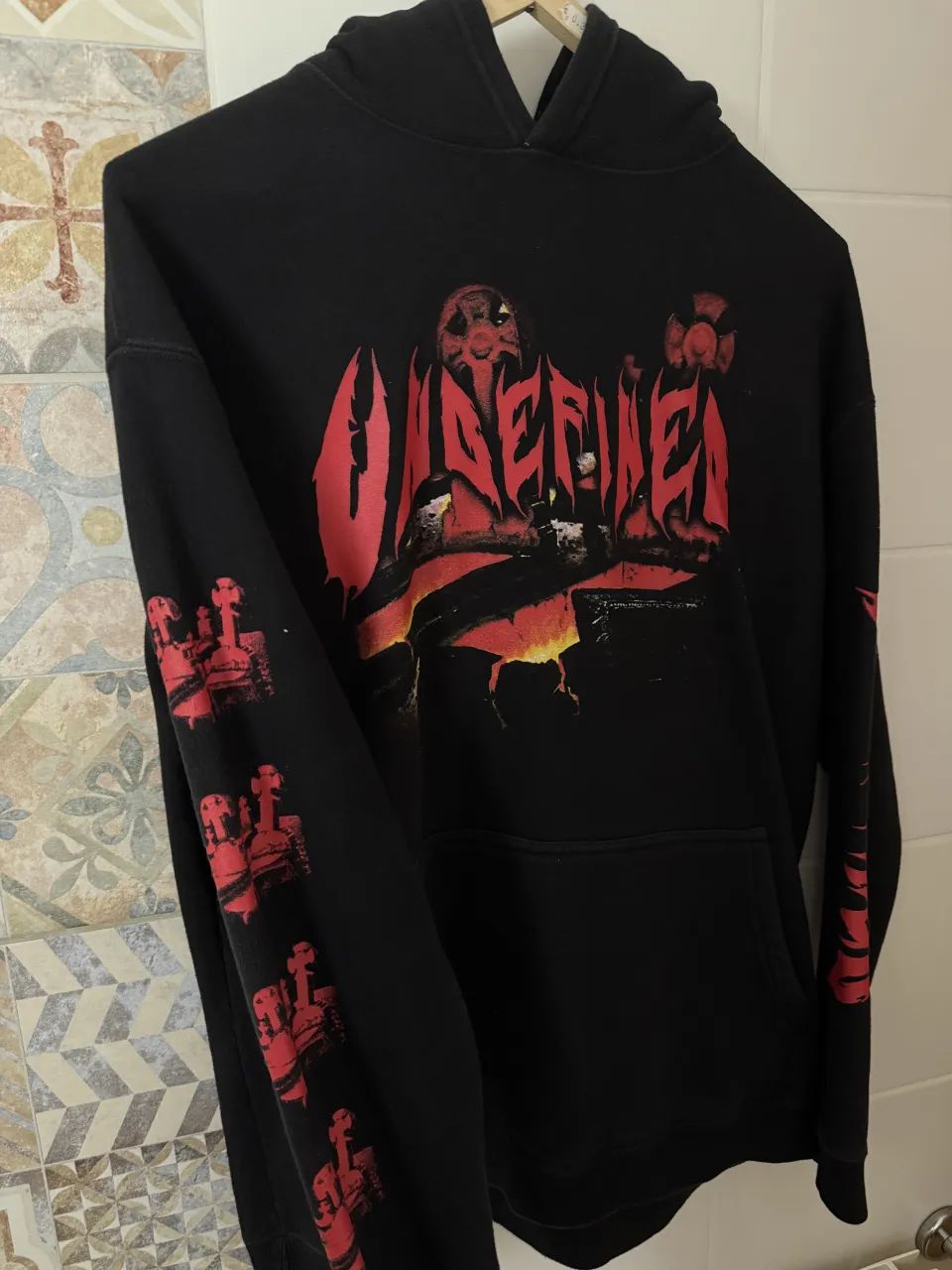 Buzo negro con capucha y estampa gráfica roja en el frente. Posee estampa de cruces rojas en ambas mangas. Etiqueta interior con la marca 'undefined'.