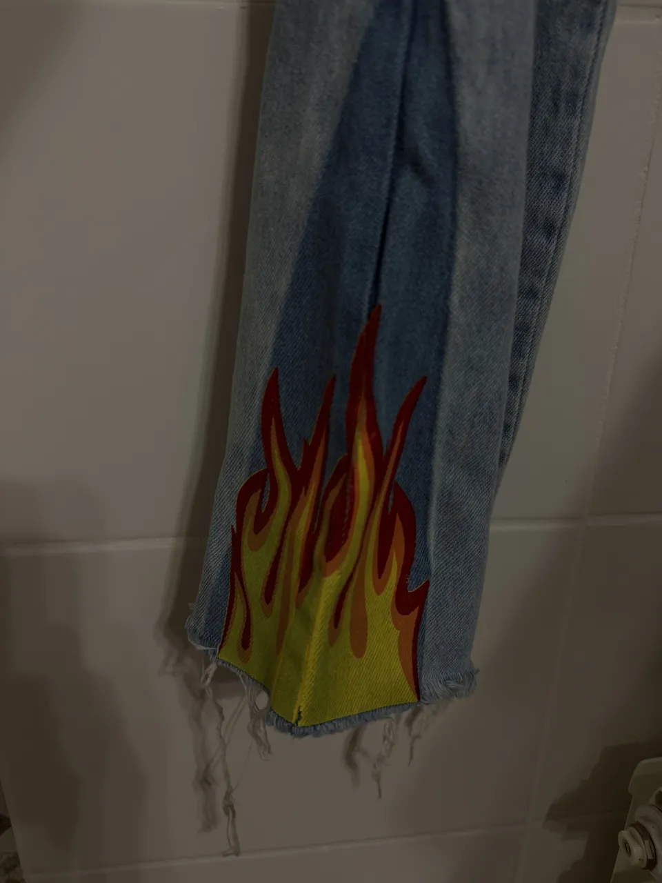 Jeans de tiro alto con estampa de llamas en los bajos y en el bolsillo trasero. Los bajos son desflecados.