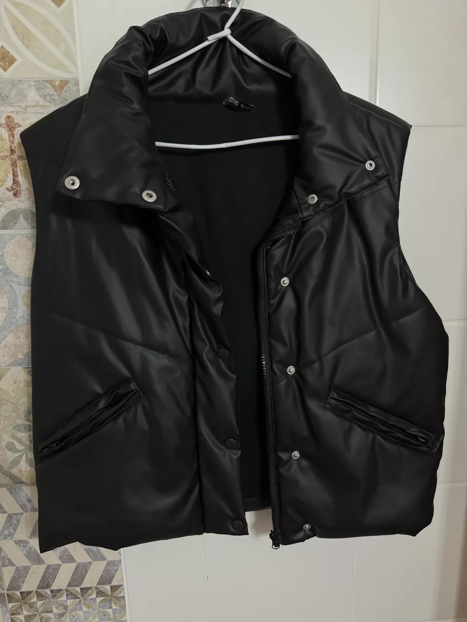 Chaleco negro acolchado con cuello alto y botones a presión en el frente. Posee bolsillos con cierre a los costados.