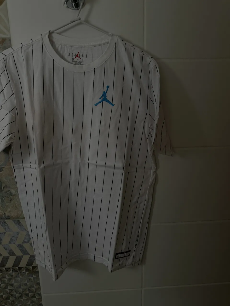 Remera blanca de manga corta con rayas verticales negras y logo de Jordan bordado en azul en el frente.