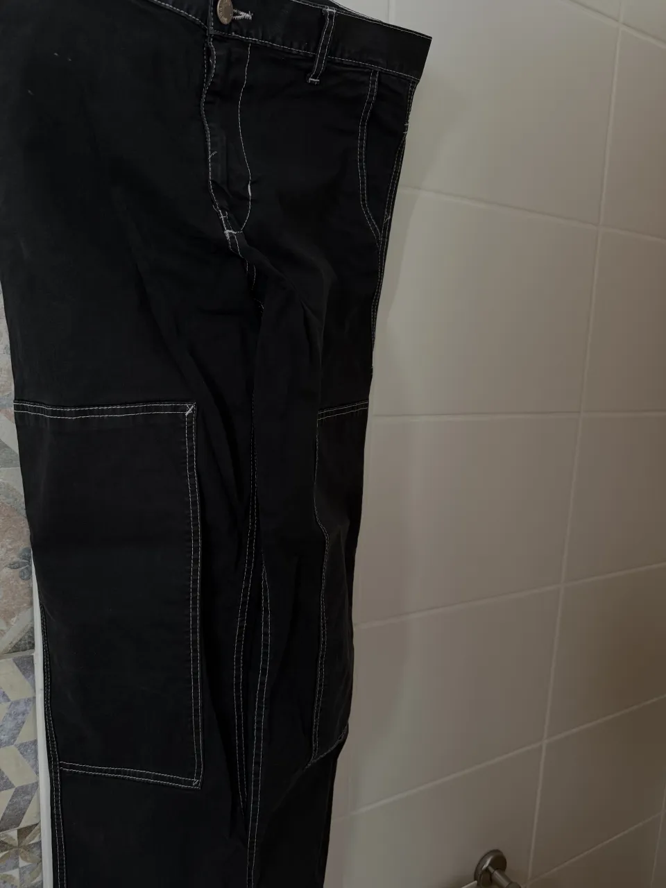 Pantalón cargo negro con pespuntes blancos. Tiene bolsillos frontales y traseros.